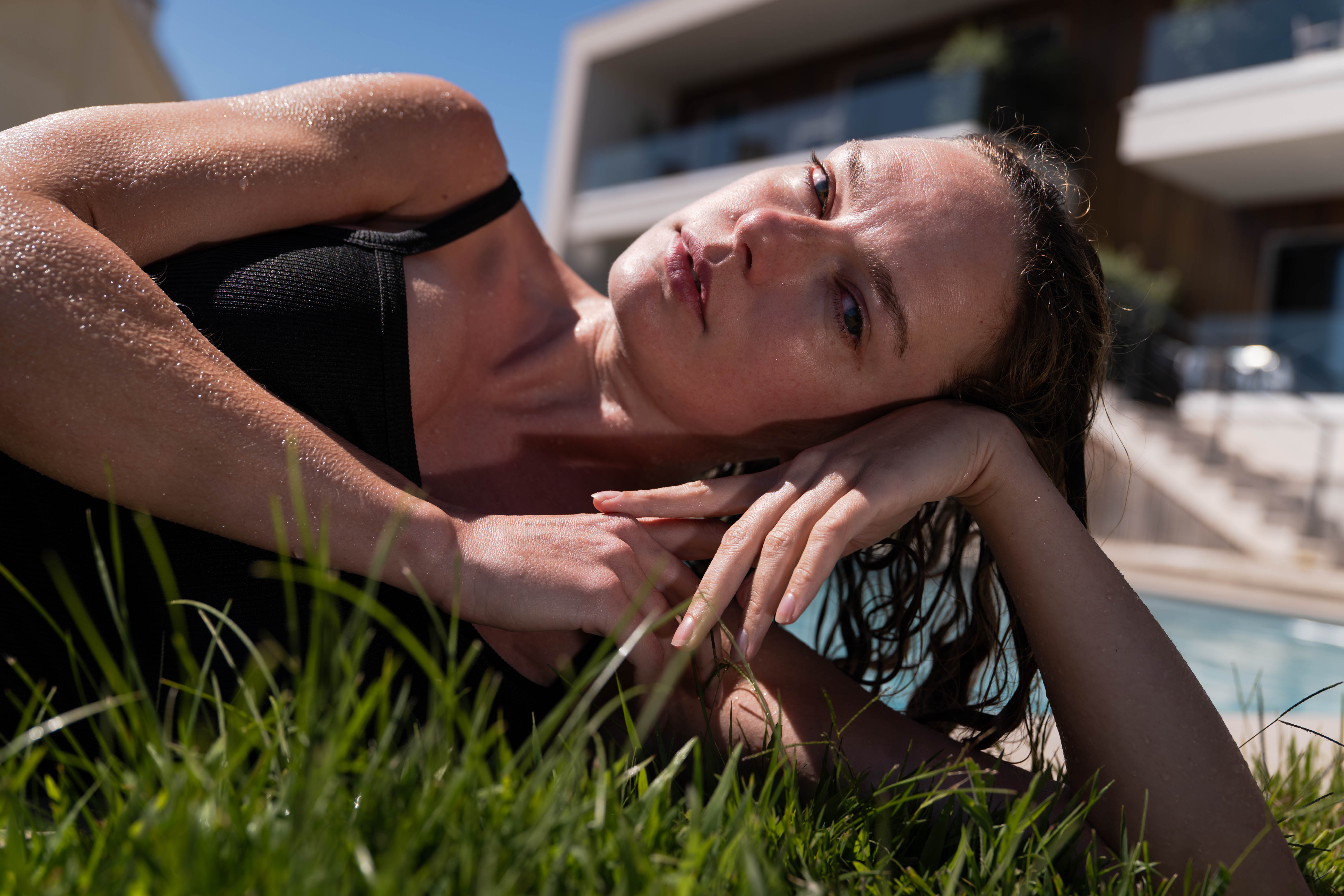 A woman resting her head on her arms on grass beside a pool